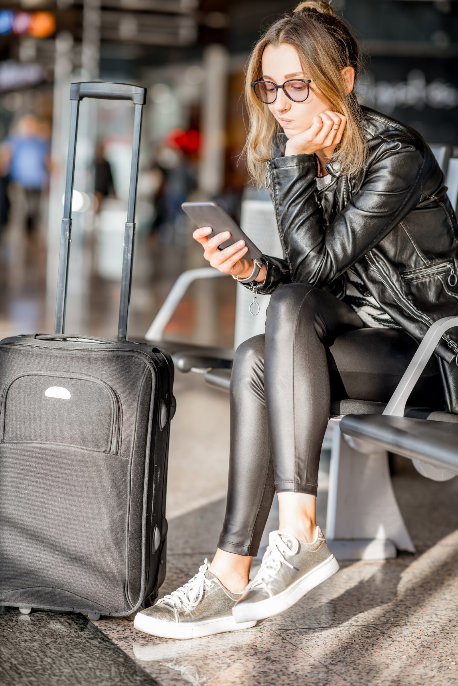 Woman sitting with phone and suitcase in an airport departure hall