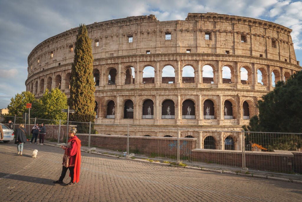 The Colosseum in Rome at sunrise with tourists and a street performer