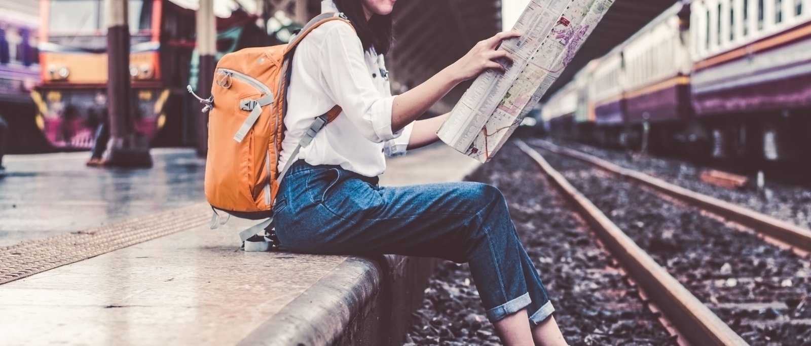 A budget traveler with a backpack holding a map while waiting for a train