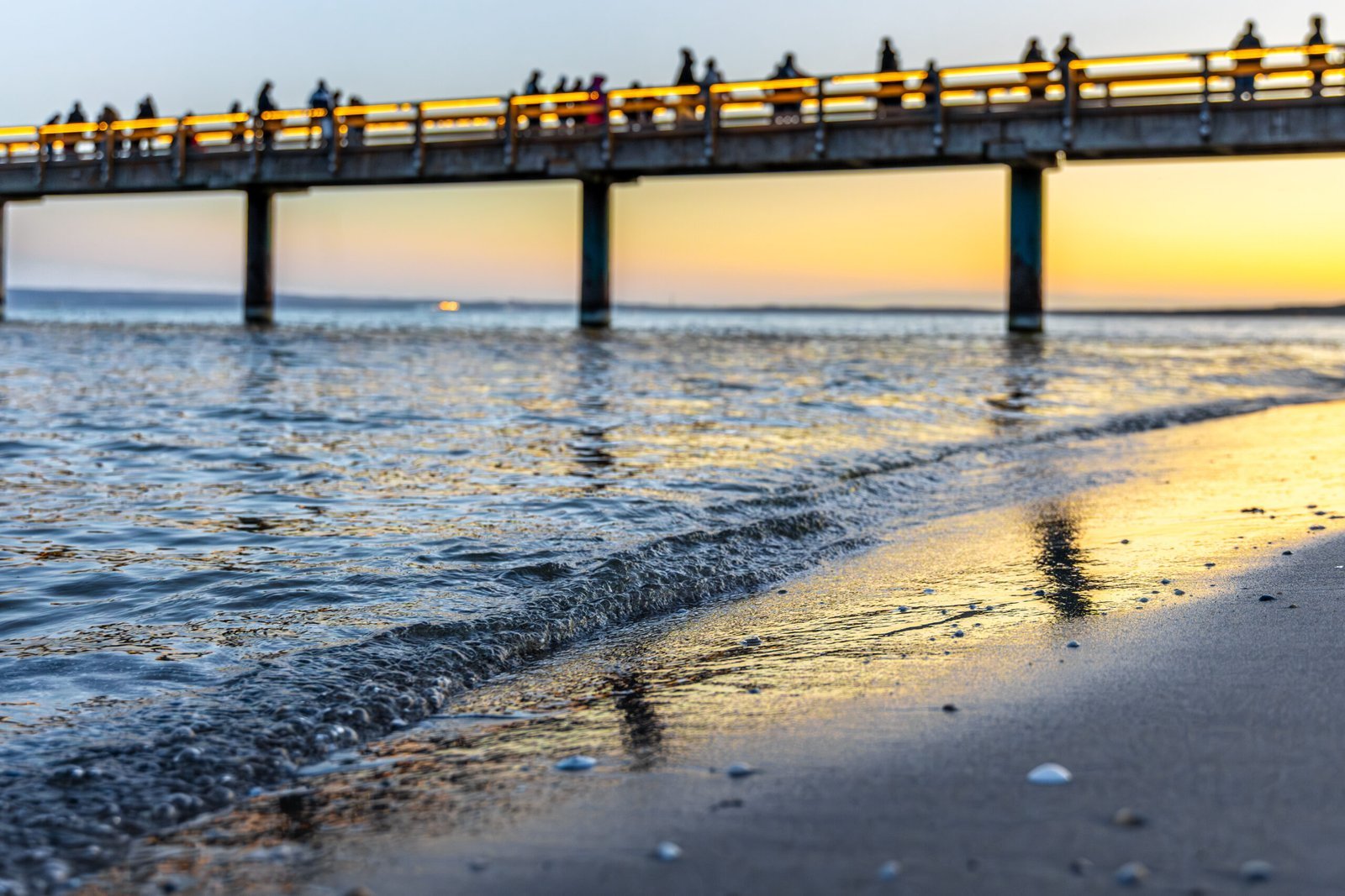 Evening pier over sea waves at sunset with people walking on boardwalk golden hour Atlantic City