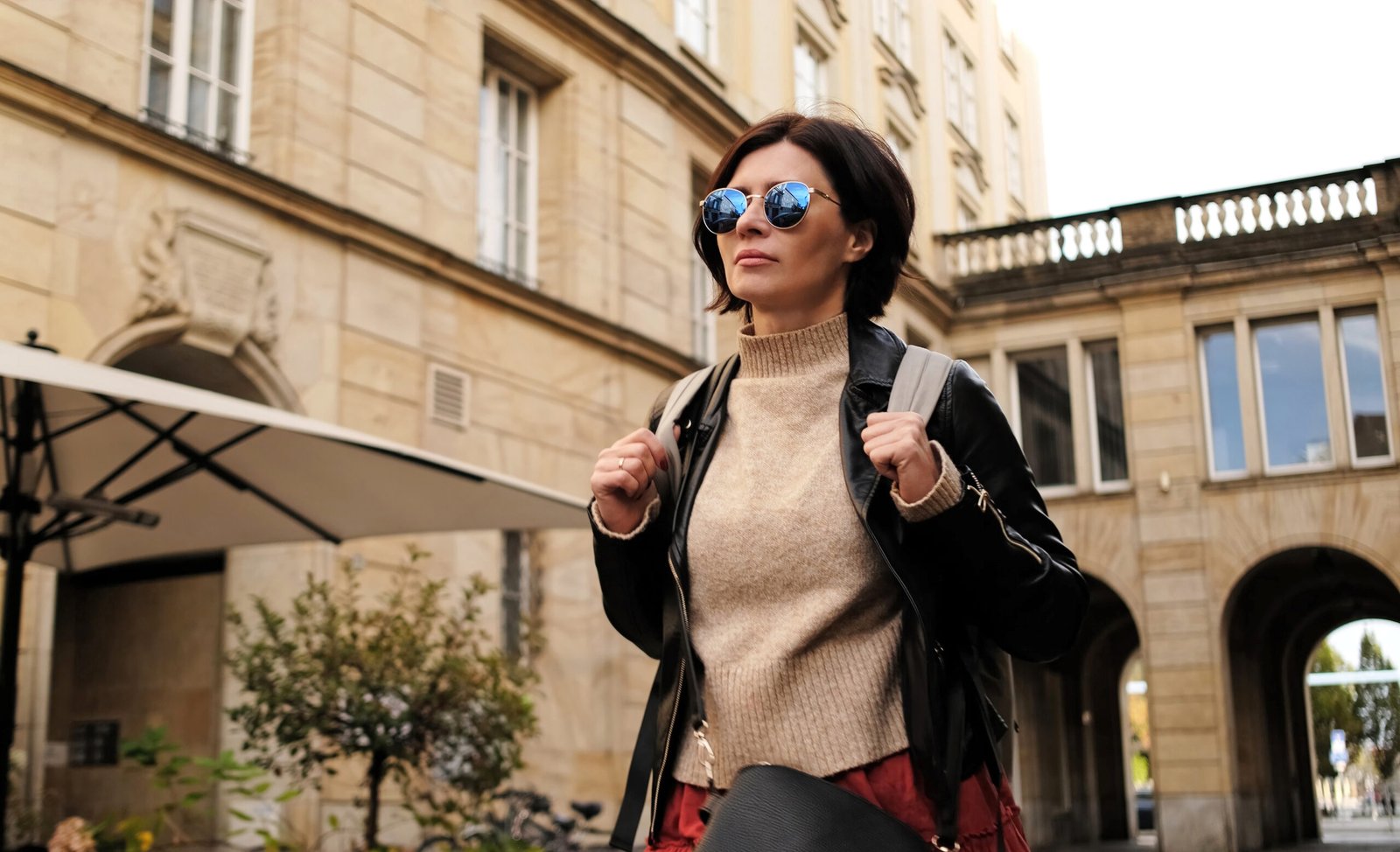 A stylish solo female traveler walking with a backpack through a city street