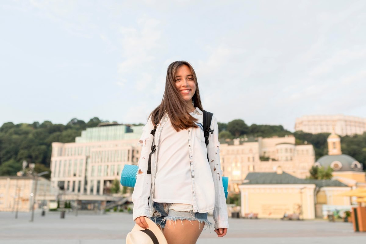 A smiling solo traveler with a backpack and hat