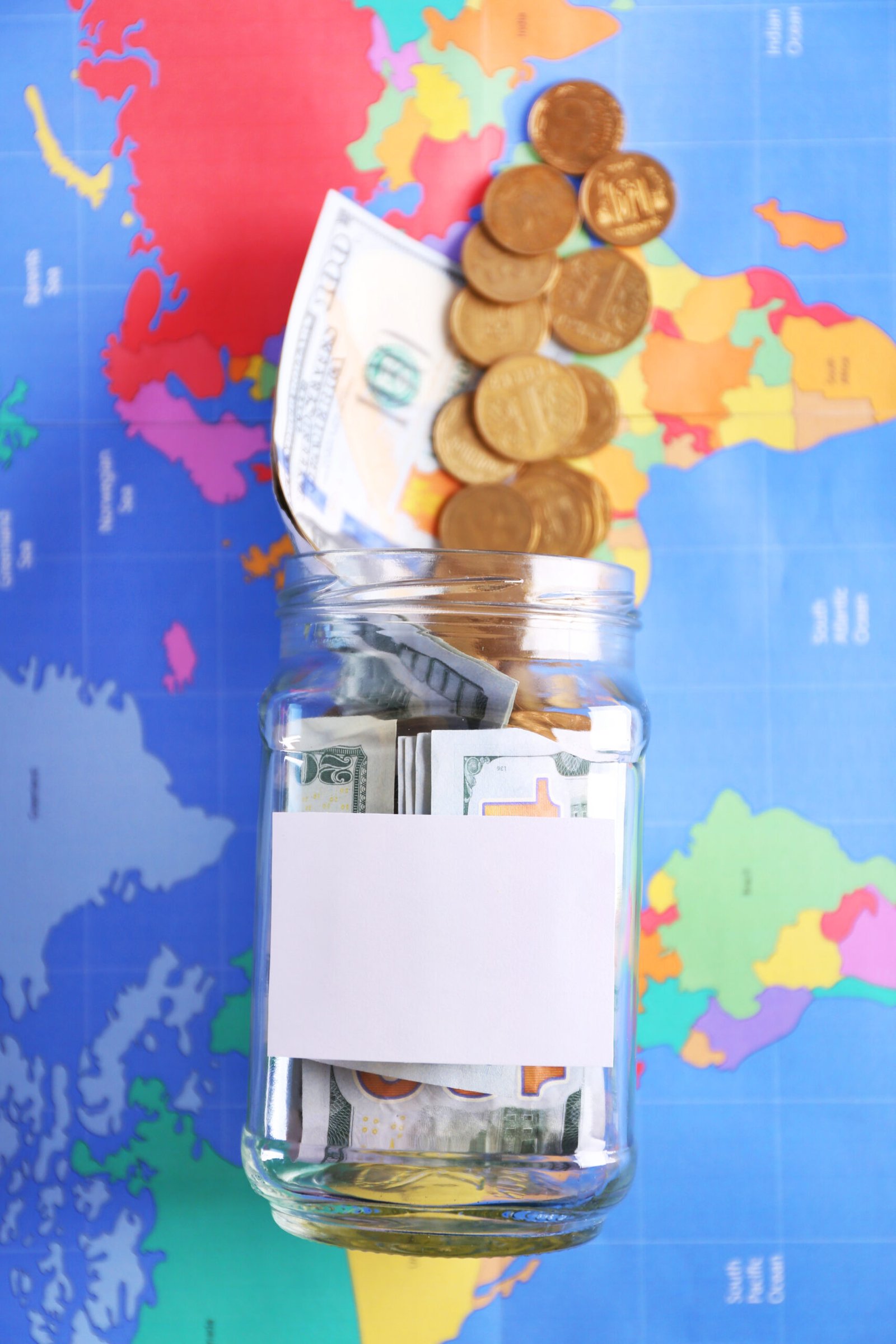 A glass jar of savings for a trip on a colorful map background
