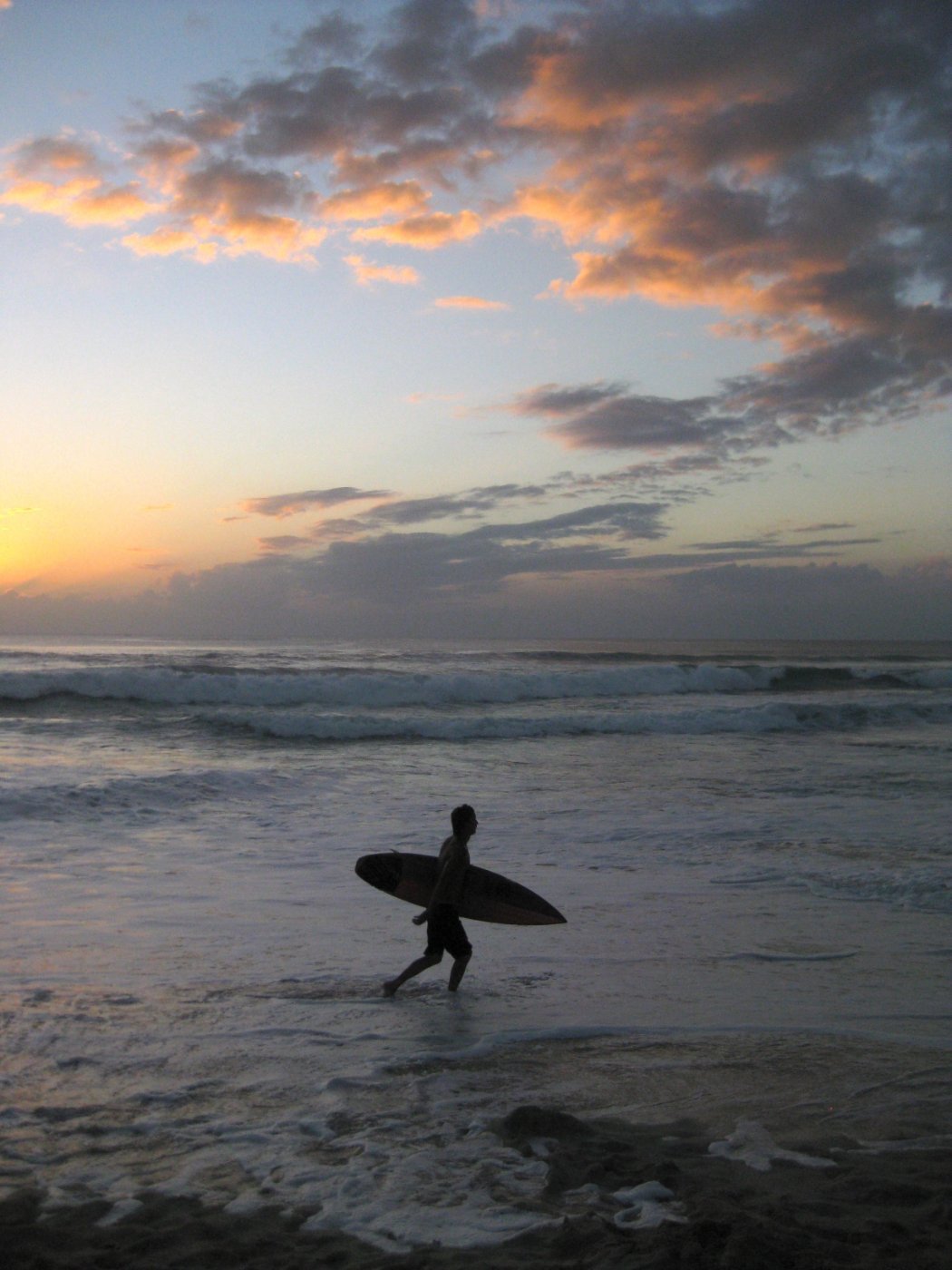 A surfer heading out at sunset