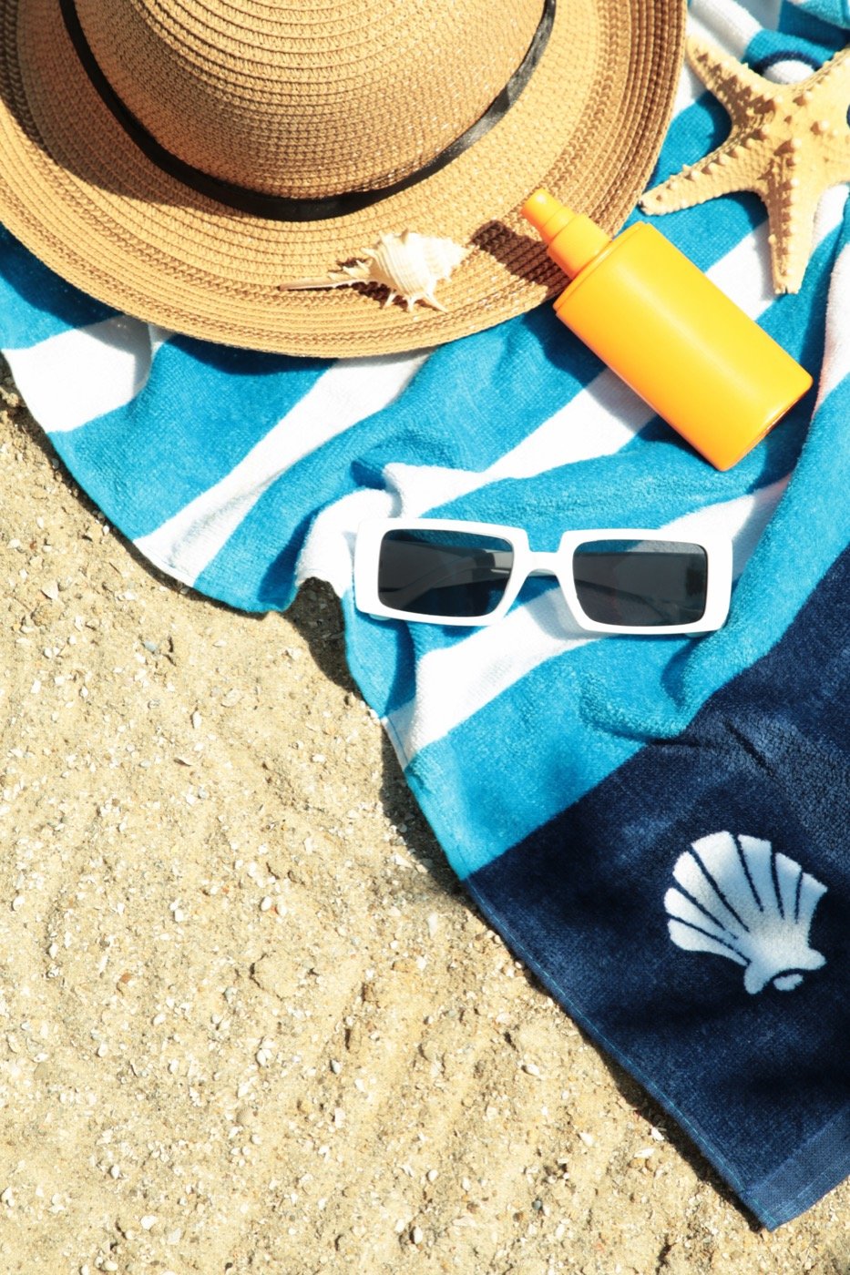 Sunscreen, sunglasses and a hat laid out on a beach towel
