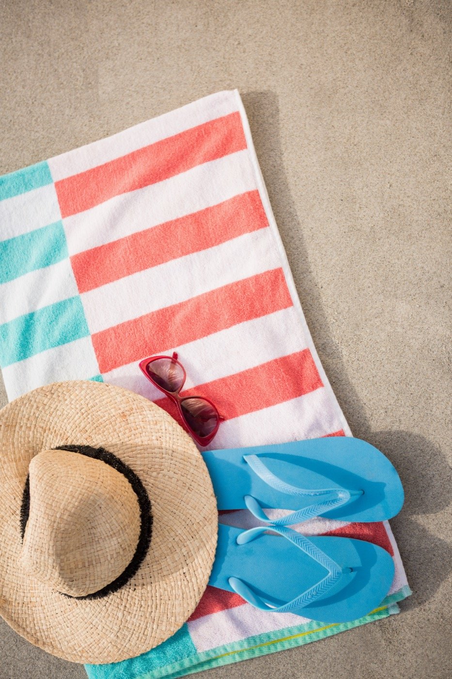 A straw hat, flip flops and sunglasses on a beach blanket