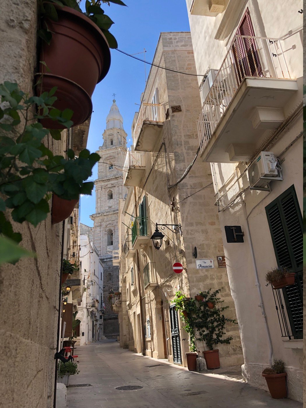 A narrow street in Monopoli with a church tower beyond