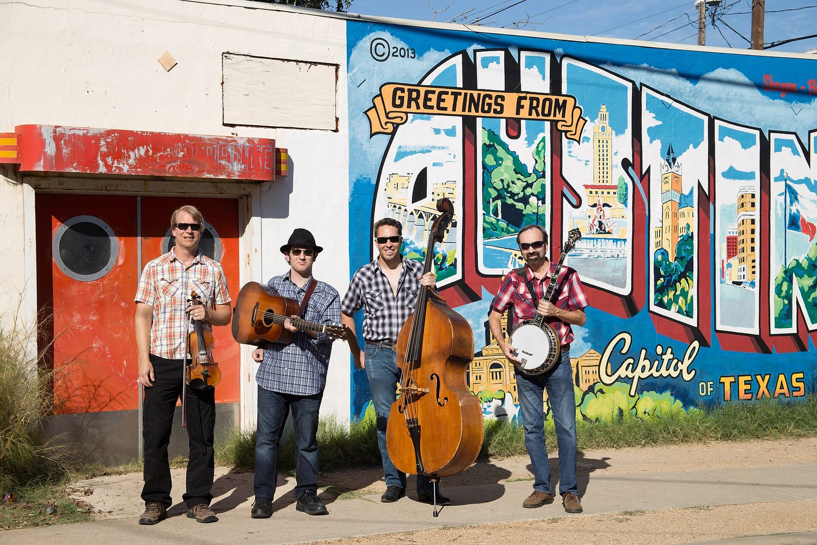A band posing in front of the Greetings from Austin postcard mural
